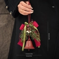 Vintage red Christmas bell with pine cones and bow held against a black coat - B-Style Red