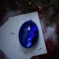 Adorno navideño azul estrellado con forma de gema facetada sobre ramas de pino nevadas - Estilo Ovalado Azul