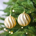 Two 8cm champagne gold Christmas balls with spiral glitter texture on a festive tree - Gold Twisted Style