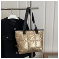 Detail der metallisch goldenen Stepptasche mit schwarzen Trägern am silbernen Metallständer - Gold
