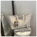 Dettaglio borsa tote color crema con ciondolo di peluche marrone su espositore - Bianco panna con pendente