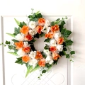 Artificial wreath with vibrant orange and white roses on a white front door background - Orange White Rose Green Leaf Style