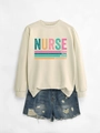 Flat lay of cream nurse sweatshirt with caring loyal strong text and denim shorts - Sand