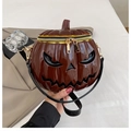 Detail showing high-gloss brown pumpkin bag with 3D镂空 classic ghost face and dual gold zippers - Brown