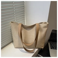 Close-up of woven straw tote bag with brown faux leather handles in a sunny setting - Khaki