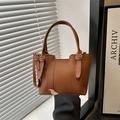 Brown litchi grain leather bucket bag with dual handles and gold hardware in hand - Brown