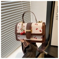 Detail van witte vierkante crossbodytas met kersenprint, brede riem en metalen hanger - koffiekleur