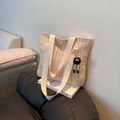 Beige geflochtene Strohtasche mit schwarzem Pompon-Anhänger auf minimalistischem Buch - Cremeweiß mit Anhänger