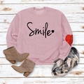 Pink crewneck sweatshirt with Smile text and heart detail shown in a cozy autumn outfit - Rose Gold (Black Font)