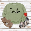 Detail of green crewneck sweatshirt with Smile print and heart accent on white wood floor - Olive Green (Black Font)