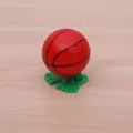 Wind-up basketball toy in red finish with green feet on wooden background - Basketball