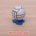 Wind-up jumping volleyball toy in white and black with blue feet on a wooden desk - Volleyball