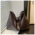 Detail of dark brown glossy leather tote bag featuring wide strap with silver metal eyelets - Coffee