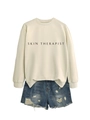 Détail d'un sweat à col rond ample avec imprimé Skin Therapist et mini short en jean troué - Sable (Police Noire)