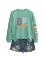 Détail d'un sweat vert menthe avec imprimé et d'un short en jean bleu à effet déchiré - Vert clair