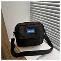 Primer plano de bolso bandolera de nailon negro con parche de logo azul en luz natural - Negro