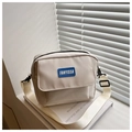 Primer plano del bolso bandolera de lona crema con logo FANYISSA en un alféizar soleado - Blanco