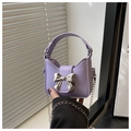 Close-up of mini purple bag with silver bow detail and metal chain strap held in hand - Purple