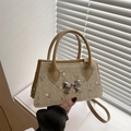 Straw handbag with floral embroidery and silver bow buckle shown in a lifestyle setting - Khaki