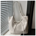 Detail view of cream-white tote bag featuring delicate woven texture and bow tie accent - White