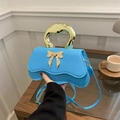Himmelblaue Handtasche mit goldenem Metallgriff und Schleifen-Detail auf Holztisch - Blau