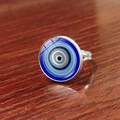 Macro shot of silver Evil Eye charm ring on a rustic reddish wood texture background - Nazar Cabochon Spherical Evil Eye Style (JY009127-10)