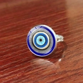 Macro shot of silver evil eye ring featuring a blue glass dome on a dark wood background - Sky Blue Concentric Evil Eye Style (JY009127-7)