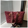 Gros plan d'un sac cabas matelassé bordeaux avec texture en losange et patchs décoratifs - Rouge