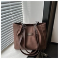 Detalle de bolso tote marrón con textura tejida y correa de hombro de cadena metálica - café
