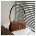 Detail of caramel brown leather handbag with gold metal clasp on white books background - Tan