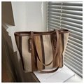Close-up of a striped canvas tote bag with brown leather handles and gold metal accents - Dark Brown