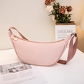 Chic light pink half-moon crossbody bag with wide shoulder strap on white tabletop - Pink