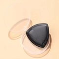 Makroaufnahme einer schwarzen dreieckigen Make-up-Quaste in einer transparenten Box - Kartonverpackung / Schwarz