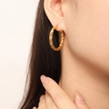Close-up of a woman wearing gold twisted rope hoop earrings with a shiny metallic finish - Twisted Rope Style (F1421) / Gold