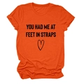 Detail eines orangenen Kurzarm-T-Shirts mit 'YOU HAD ME AT FEET' Druck und Herzmotiv - S / Oberteile / Orange (Schwarze Schrift)