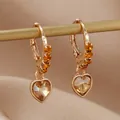 Vue détaillée de boucles d'oreilles cœur dorées avec cristaux ambrés sur tissu de soie - Jaune Doré