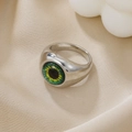 Macro shot of silver alloy evil eye ring with green iris detail on silk fabric - Silver Green Round Pupil