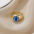 Detailansicht des goldenen Evil-Eye-Rings auf Seidenstoff mit blau-violettem Iris-Muster - Gold Blau Schlitzpupille