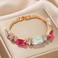 Bracelet en maille dorée avec pierres précieuses colorées sur un présentoir de luxe - Rose rouge