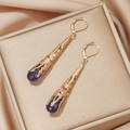 Detailopname van vintage goudkleurige oorbellen met paarse edelstenen en filigraan - Saffierblauw