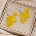 Detail view of yellow acrylic stegosaurus earrings on elegant champagne satin - Yellow Stegosaurus