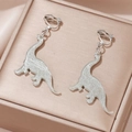 Macro detail of silver dinosaur ear clips with unique cracked texture on a jewelry box - Silver Crackle Long-neck Dinosaur