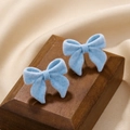 Detail view of light blue flocked bow earrings on elegant wooden stand with silk background - Blue Bow