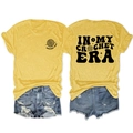 Dettaglio della stampa In My Crochet Era su t-shirt gialla e pantaloncini di jeans strappati - Giallo (Motivo nero)
