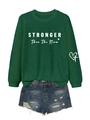Close-up of STRONGER Than The Storm print on green sweatshirt and distressed denim shorts - Vintage Green