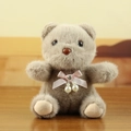 Plush brown bear keychain with pink satin bow and pearl accent on wooden background - Gray
