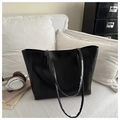 Detail of a black leather tote bag placed on a white fabric sofa in a cozy lifestyle setting - Black