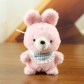 Cute pink plush bear keychain with a blue checkered lace bib on a warm wooden table - F Rabbit