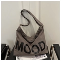Détail d'un sac bandoulière en toile grise avec lettrage MOOD posé sur une chaise noire - Gris