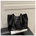 Schwarze Shopper-Tasche aus glänzendem Lackleder mit Kettenriemen auf modernem Stuhl - Schwarz